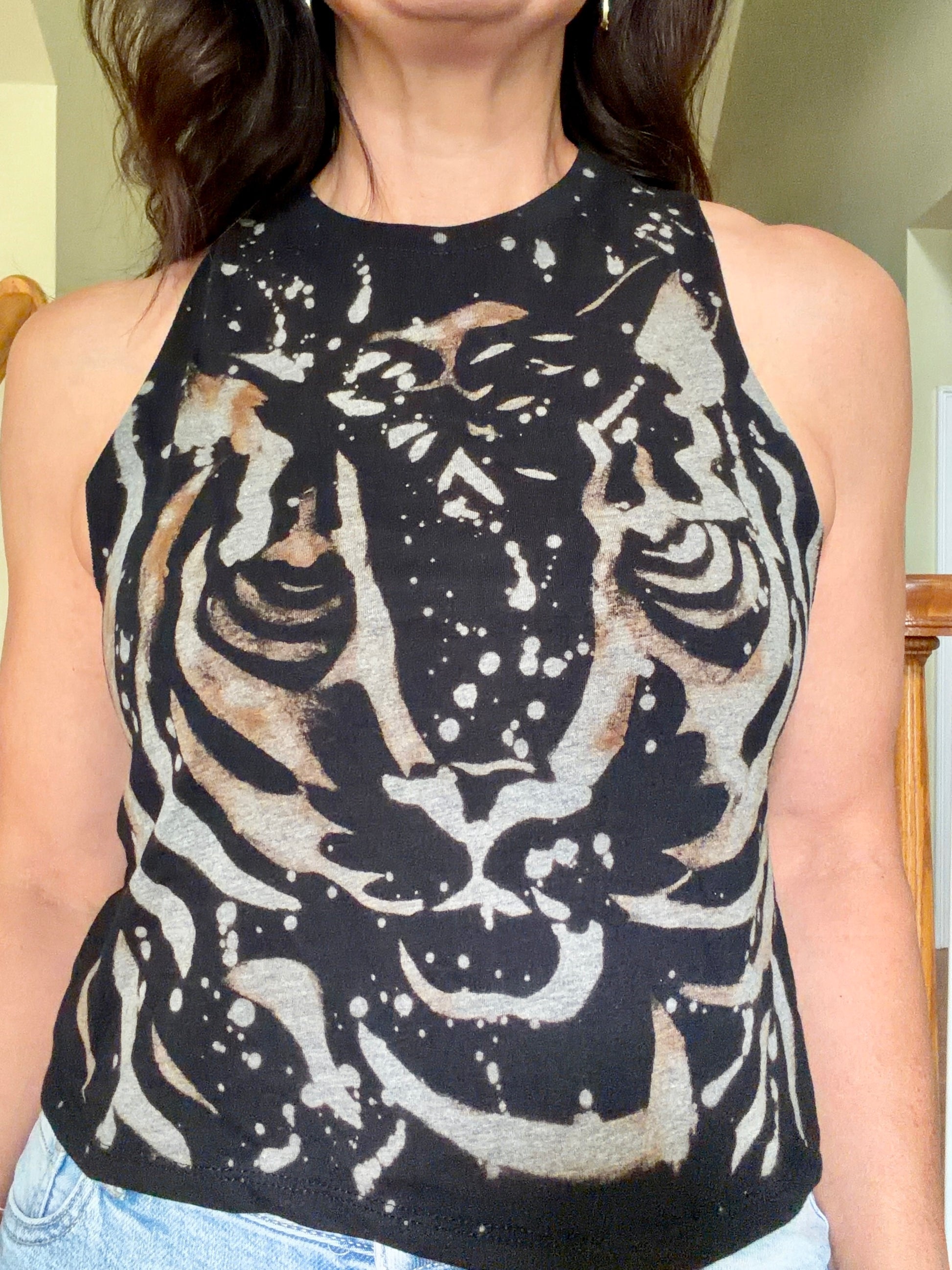 A sleeveless black knit top with a large distressed tiger face print in beige and white, worn by a model.