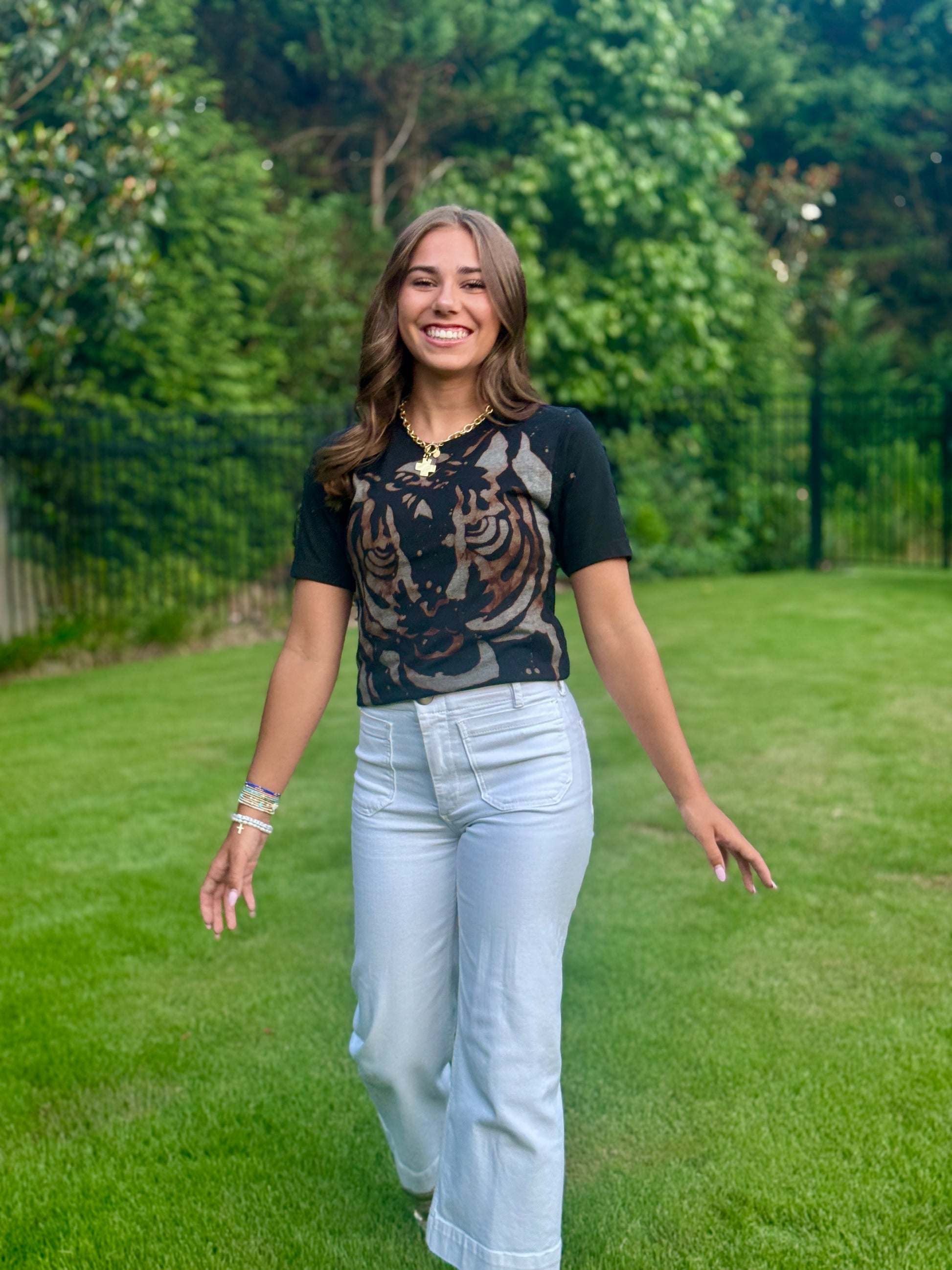 Woman standing in a grassy area with trees in the background wearing tiger design t-shirt