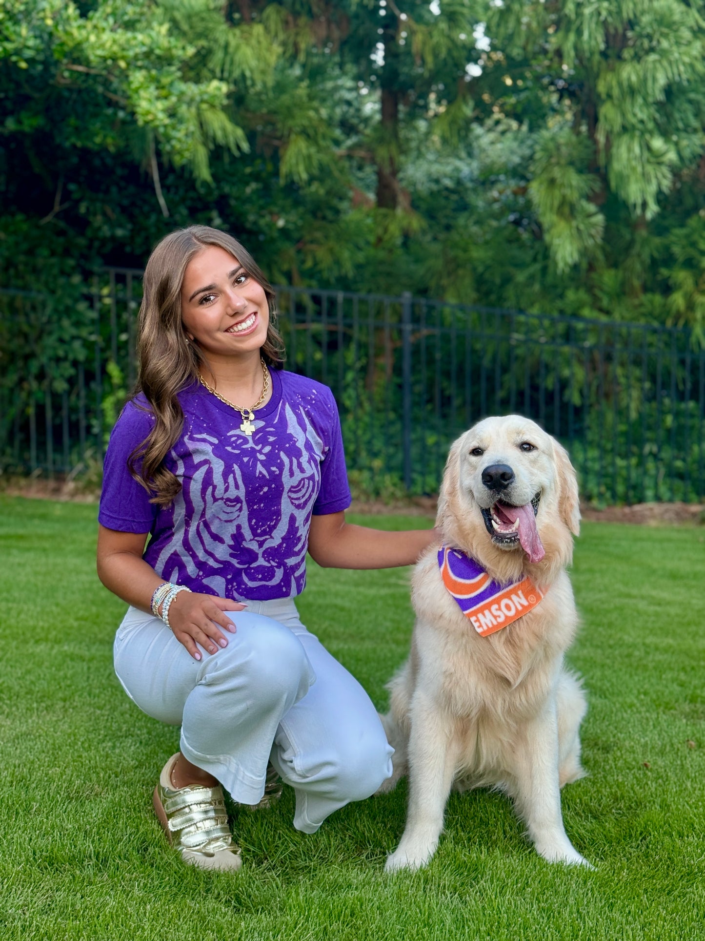 Woman in a purple shirt with a tiger design and a dog wearing a bandana in a park setting.